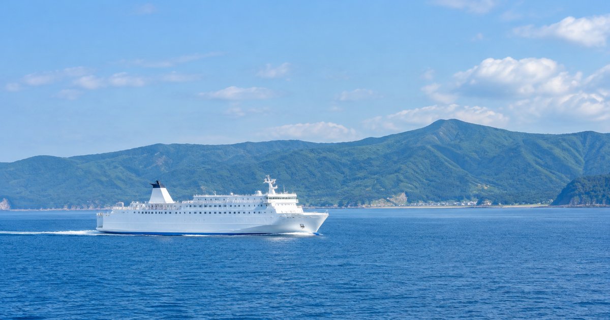 晴れた日の津軽海峡を渡る白いフェリーと、緑の山が続く青森の海岸