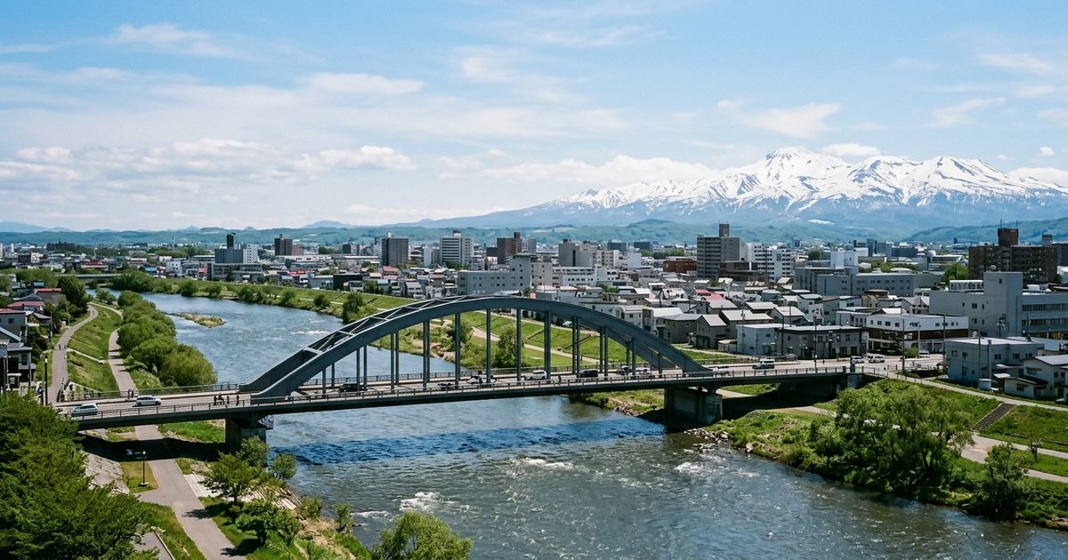 旭川の街を流れる川に架かるアーチの橋と、遠くの雪をかぶった大雪山の山並み